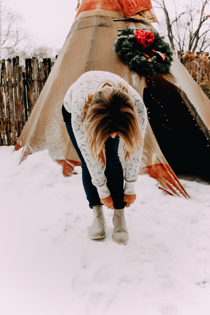 How To Cuff Women's Jeans featured by top US fashion blogger Audrey Madison Stowe; Woman standing in front of tepee wearing a sweater and jeans.