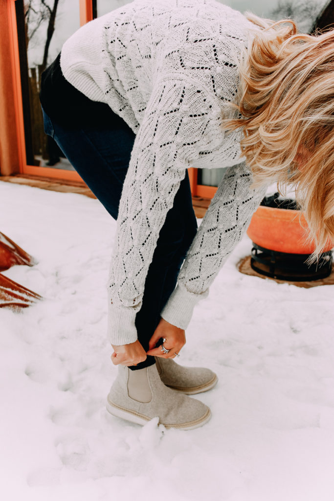 How To Cuff Women's Jeans featured by top US fashion blogger Audrey Madison Stowe; Woman standing in front of tepee wearing a sweater and jeans.