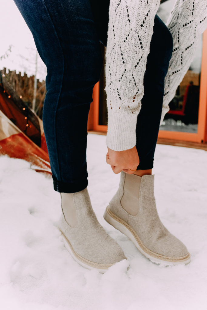 How To Cuff Women's Jeans featured by top US fashion blogger Audrey Madison Stowe; Woman standing in front of tepee wearing a sweater and jeans.