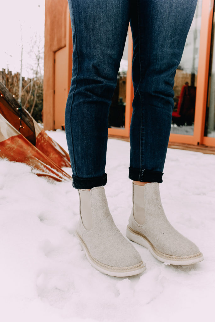 How To Cuff Women's Jeans featured by top US fashion blogger Audrey Madison Stowe; Woman standing in front of tepee wearing a sweater and jeans.